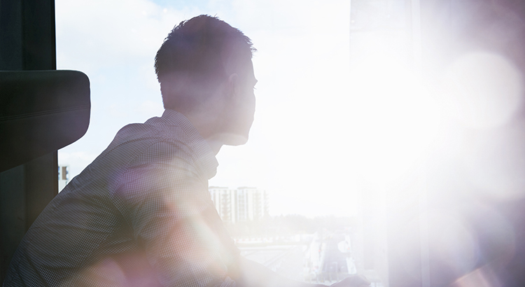 silhouette of man looking out window with flare